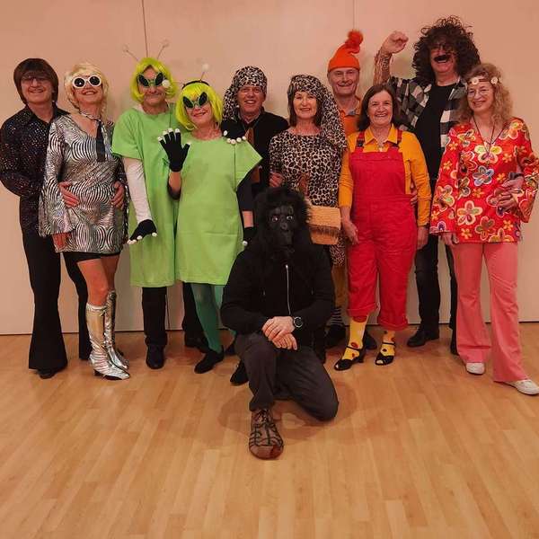Eine Gruppe von Tänzern posiert in verschiedenen Mottokostümen, darunter Hippie, Disco und Alien TANZKURS FÜR EIN MOTTO / THEMA