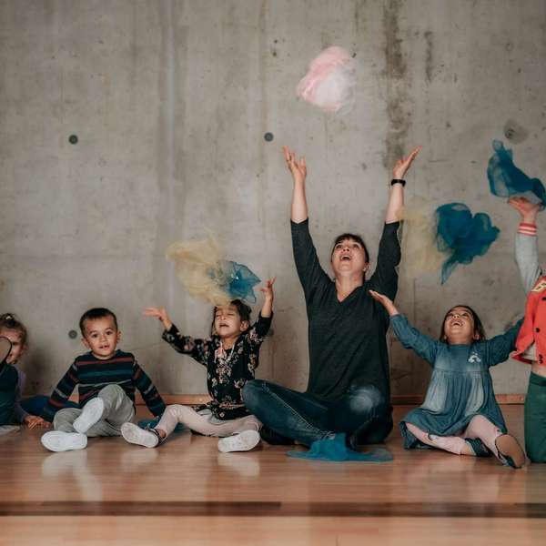 Eine Tanzlehrerin und eine Gruppe von Kindern spielen fröhlich mit bunten Tüchern in einem Kindertanzkurs Kindertanzkurs – Spiel & Spaß bei Tanzschule No.10