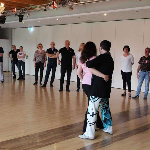 Ein Tanzlehrerpaar demonstriert einen Tanzschritt vor einer Gruppe von Schülern in einem Tanzstudio TANZKURS FÜR PRIVATE GRUPPEN