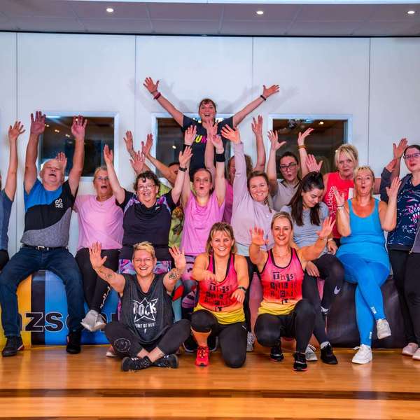 ine fröhliche Gruppe von Teilnehmern posiert nach einem Fitnesskurs in der Tanzschule No.10, die Hände in der Luft Fitness-Kurse bei Tanzschule No.10 – Dein Training für mehr Energie und Spaß