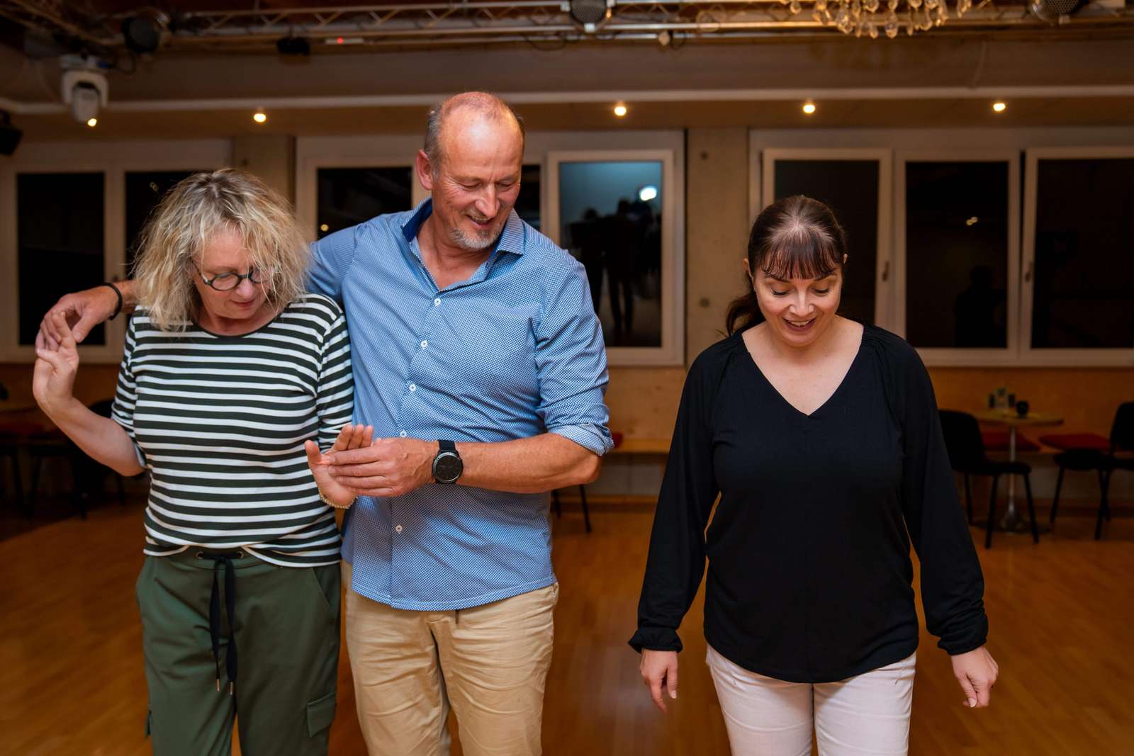 Drei Erwachsene nehmen an einer Tanzstunde teil und lernen die Grundlagen des Paartanzes